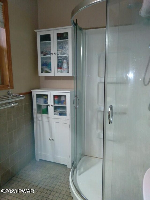 bathroom featuring tile patterned floors, a shower with door, and tile walls