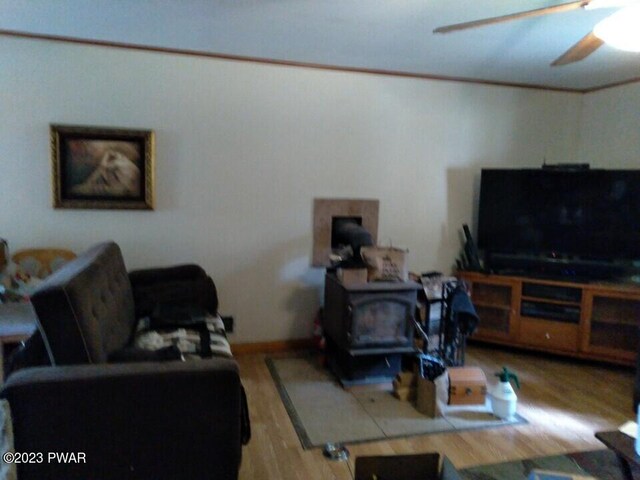 living room with light hardwood / wood-style flooring, a wood stove, ceiling fan, and crown molding