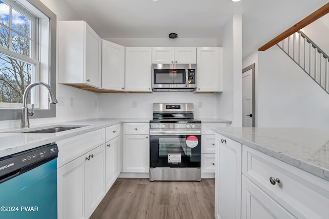 kitchen with white cabinets, appliances with stainless steel finishes, light stone counters, and sink