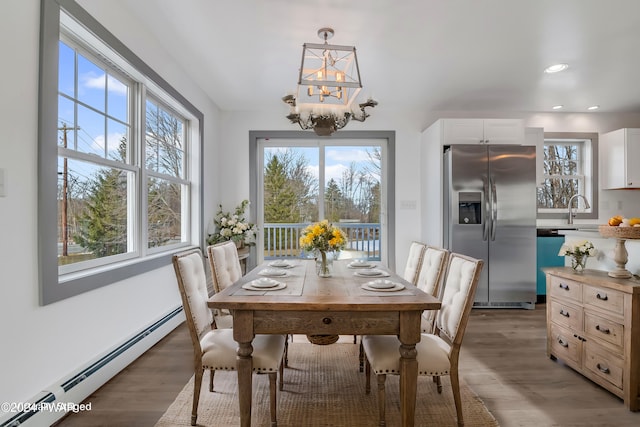 dining area featuring dark hardwood / wood-style flooring, baseboard heating, a notable chandelier, and sink