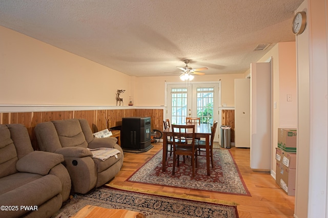 127 E Mulberry Dr, Milford, PA 18337 - dining space featuring a textured ceiling, a ceiling fan, light wood finished floors, a wainscoted wall, and a wood stove