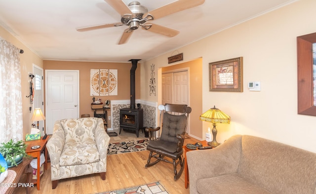 sitting room with hardwood / wood-style floors, ornamental molding, ceiling fan, and a wood stove