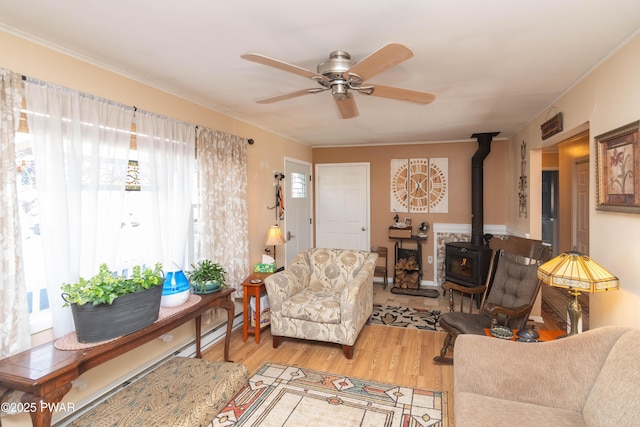 living room featuring light hardwood / wood-style flooring, ornamental molding, ceiling fan, and a wood stove