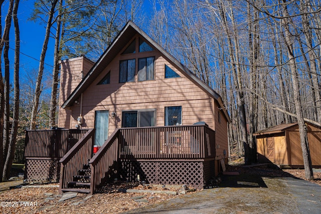 rear view of property featuring a deck, an outdoor structure, and a storage unit