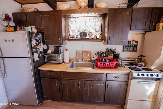 kitchen with dark brown cabinets, white range with electric cooktop, light countertops, freestanding refrigerator, and a sink