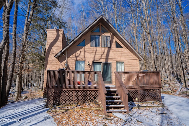 snow covered back of property with a chimney and a deck