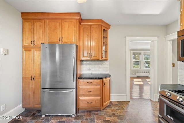 kitchen with backsplash, radiator heating unit, stainless steel appliances, and dark stone counters