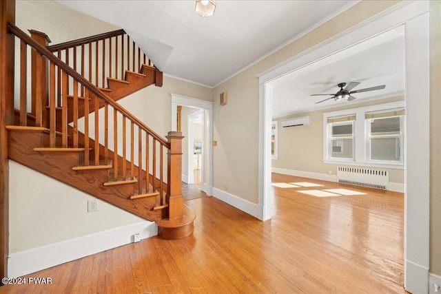 foyer featuring ceiling fan, radiator heating unit, a wall unit AC, light hardwood / wood-style floors, and ornamental molding