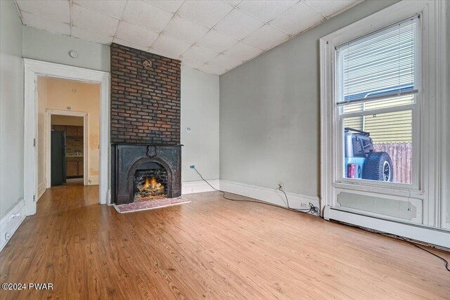 unfurnished living room featuring a drop ceiling, wood-type flooring, plenty of natural light, and a brick fireplace