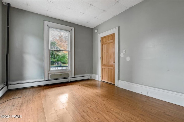 empty room with a baseboard radiator, a drop ceiling, and light hardwood / wood-style floors