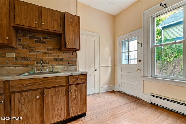 kitchen with backsplash, a baseboard radiator, light hardwood / wood-style floors, and sink