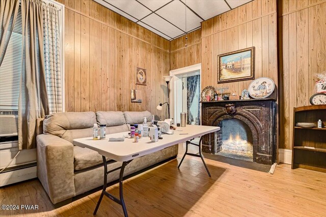 sitting room featuring light wood-type flooring, a paneled ceiling, and wood walls