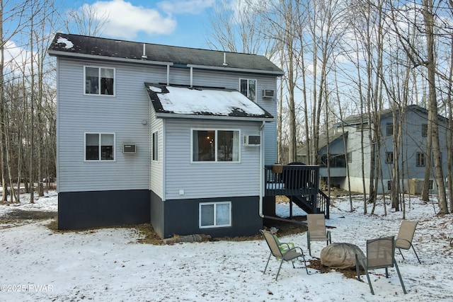 snow covered rear of property featuring a deck, a fire pit, and a wall mounted air conditioner