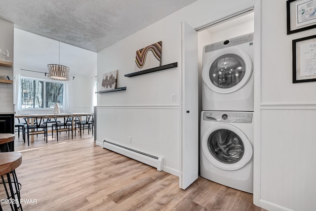 clothes washing area featuring stacked washing maching and dryer, an inviting chandelier, light hardwood / wood-style flooring, and a baseboard radiator