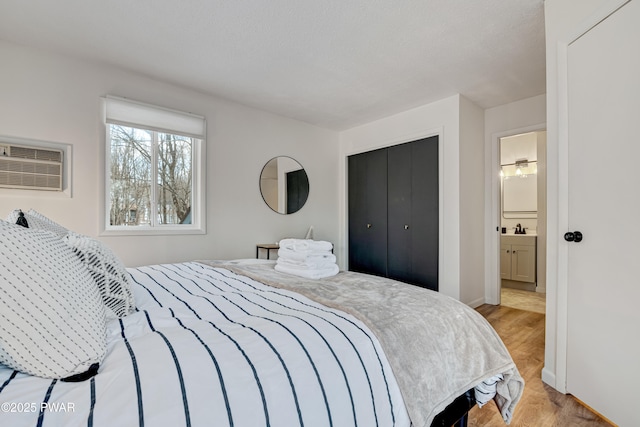 bedroom with light hardwood / wood-style floors, sink, a wall mounted air conditioner, connected bathroom, and a closet