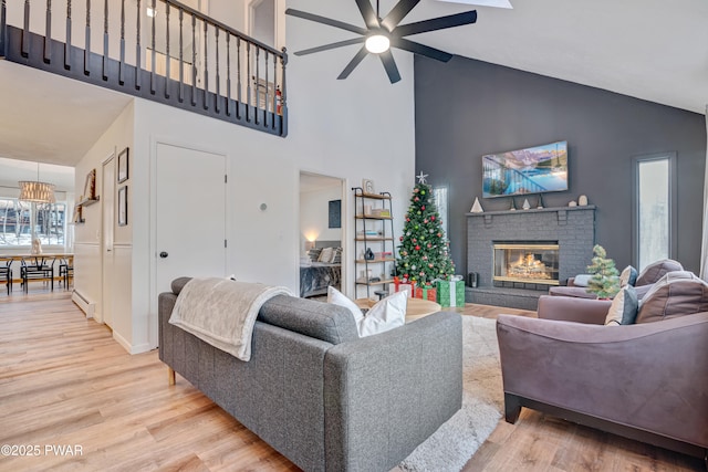 living room featuring a baseboard heating unit, a fireplace, light hardwood / wood-style floors, ceiling fan, and high vaulted ceiling