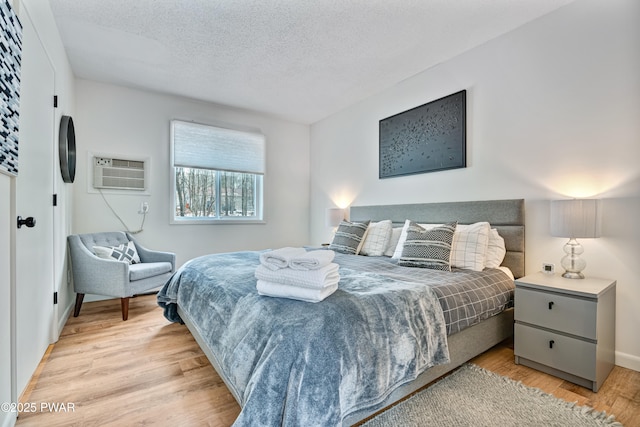 bedroom featuring light hardwood / wood-style floors, a textured ceiling, and a wall mounted AC