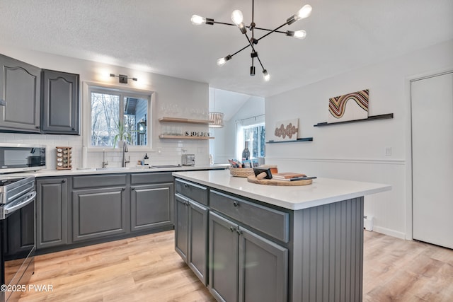 kitchen featuring a kitchen island, a healthy amount of sunlight, light wood-type flooring, gray cabinetry, and stainless steel appliances