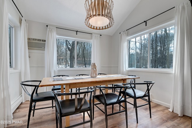 dining room featuring a wall mounted AC, vaulted ceiling, a baseboard heating unit, and light hardwood / wood-style flooring