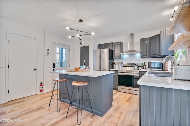 kitchen with wall chimney range hood, a kitchen island, sink, appliances with stainless steel finishes, and gray cabinetry