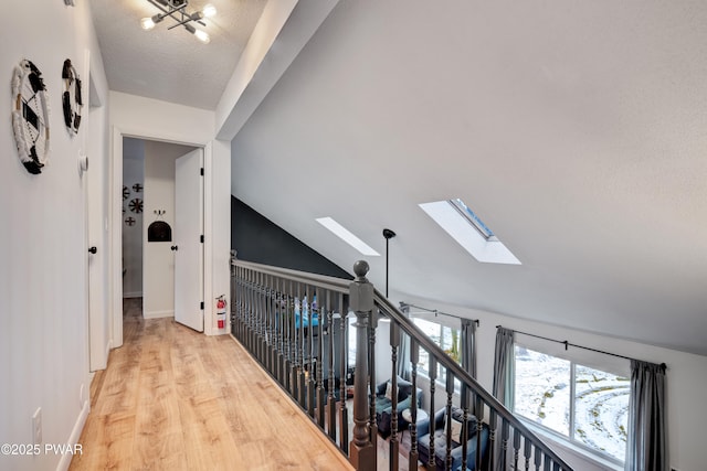 hall with a textured ceiling, light hardwood / wood-style flooring, an inviting chandelier, and vaulted ceiling