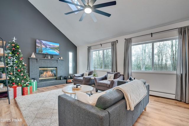 living room with a brick fireplace, ceiling fan, light wood-type flooring, baseboard heating, and vaulted ceiling