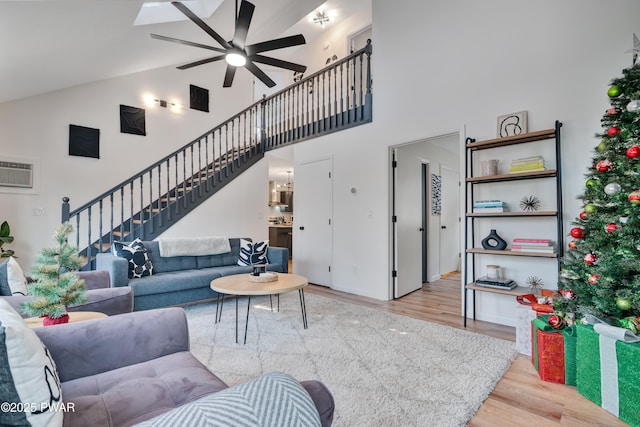 living room featuring a skylight, a wall mounted AC, ceiling fan, high vaulted ceiling, and light hardwood / wood-style flooring