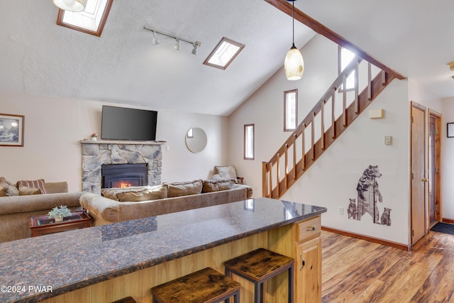 kitchen with track lighting, lofted ceiling with skylight, wood-type flooring, a stone fireplace, and hanging light fixtures