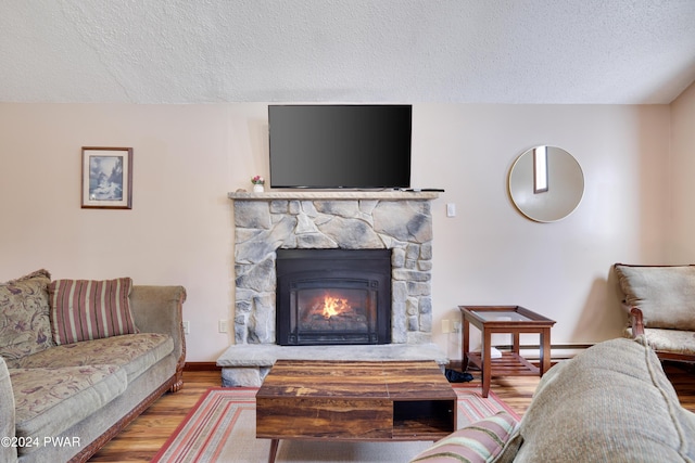 living room featuring a stone fireplace, light hardwood / wood-style floors, and a textured ceiling