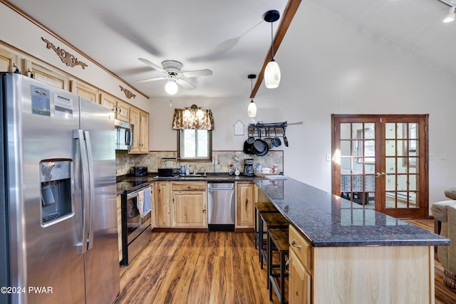 kitchen with dark stone counters, hardwood / wood-style flooring, appliances with stainless steel finishes, tasteful backsplash, and decorative light fixtures