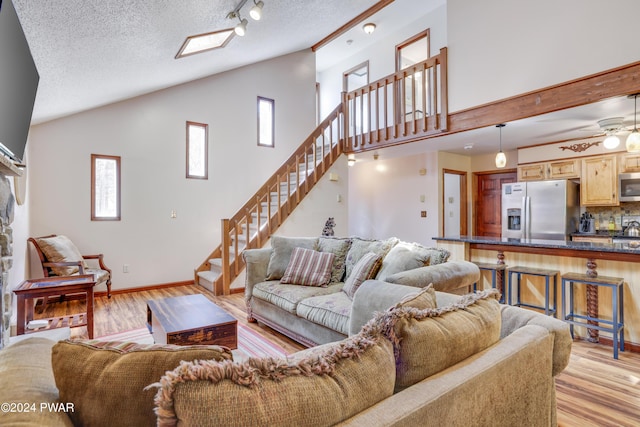 living room with a textured ceiling, light hardwood / wood-style flooring, ceiling fan, and lofted ceiling