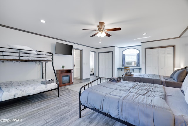 bedroom with hardwood / wood-style floors, two closets, ceiling fan, and ornamental molding