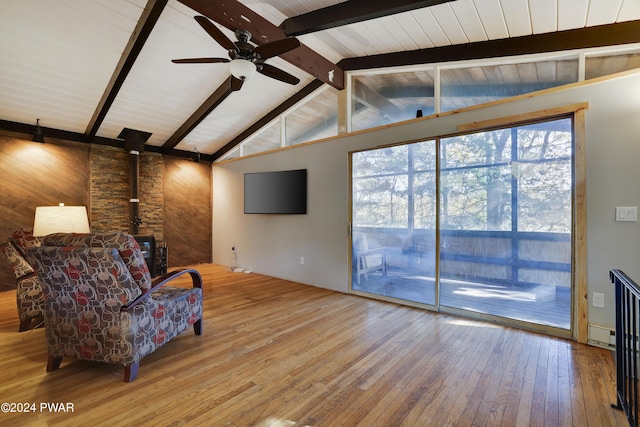 sitting room with a wood stove, wooden walls, hardwood / wood-style flooring, vaulted ceiling with beams, and ceiling fan