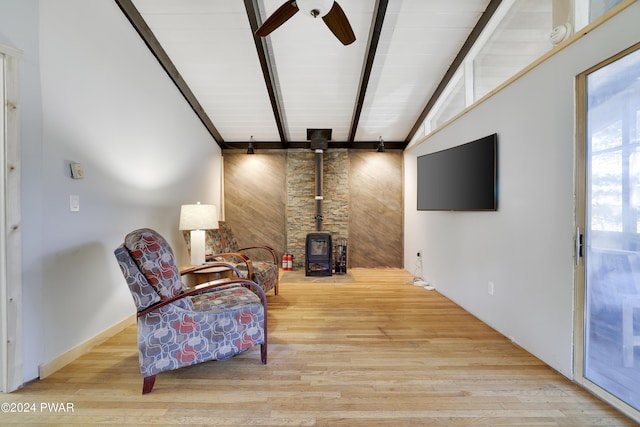 living area with a wood stove, ceiling fan, beamed ceiling, light hardwood / wood-style floors, and wooden walls