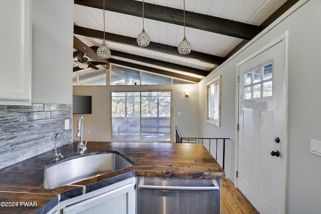 kitchen featuring butcher block counters, white cabinetry, sink, vaulted ceiling with beams, and decorative backsplash