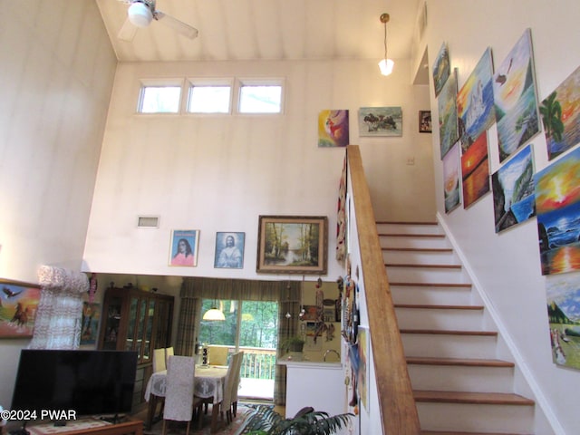 staircase featuring ceiling fan, a healthy amount of sunlight, and a high ceiling