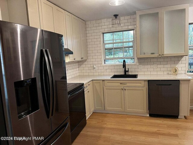 kitchen with light wood-type flooring, tasteful backsplash, sink, black appliances, and white cabinetry