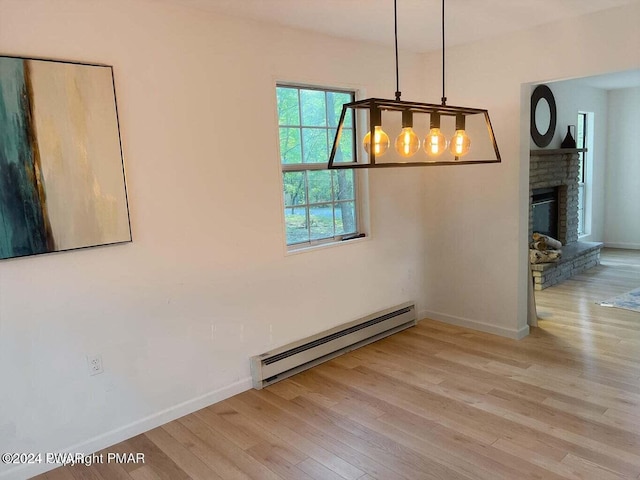 unfurnished dining area featuring a brick fireplace, light wood-type flooring, and a baseboard heating unit