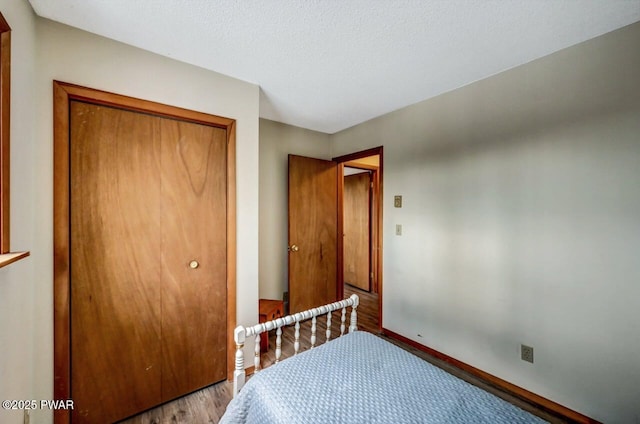 bedroom with a closet, baseboards, a textured ceiling, and wood finished floors