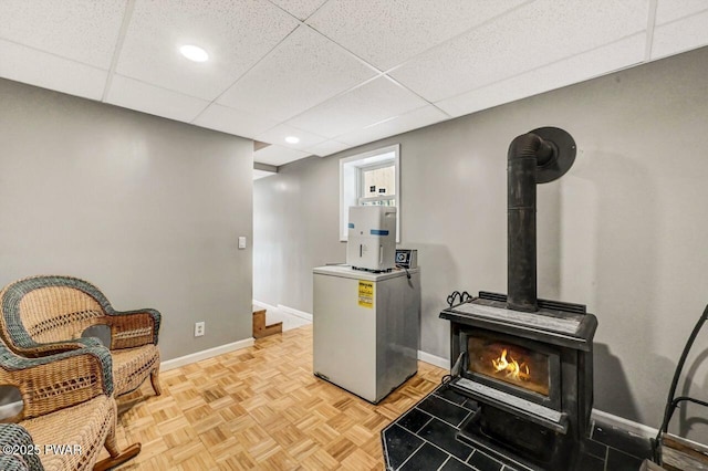 sitting room featuring stairs, a wood stove, baseboards, and a drop ceiling