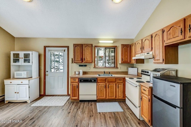 kitchen featuring white appliances, a sink, vaulted ceiling, under cabinet range hood, and light wood-type flooring