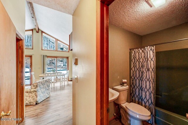 full bathroom featuring vaulted ceiling with beams, a textured ceiling, toilet, and wood finished floors