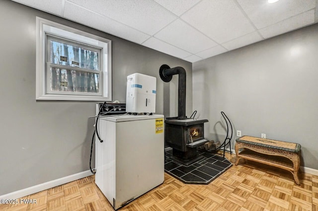 interior space with a paneled ceiling, baseboards, washer / clothes dryer, and a wood stove