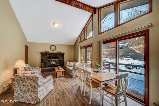 dining space featuring a brick fireplace, beamed ceiling, baseboard heating, wood finished floors, and high vaulted ceiling