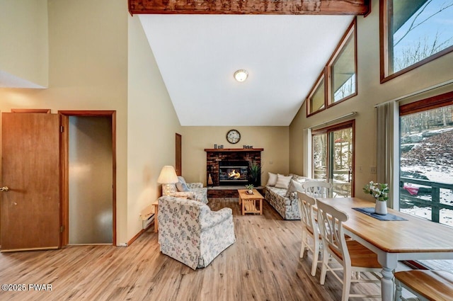 living area with high vaulted ceiling, light wood-style flooring, a baseboard heating unit, a fireplace, and baseboards