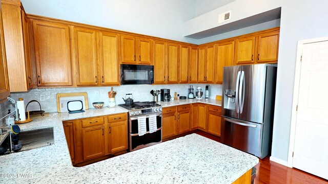 504 St Ives Ct, Bushkill, PA 18324 - kitchen featuring appliances with stainless steel finishes, brown cabinets, tasteful backsplash, light stone countertops, and a peninsula