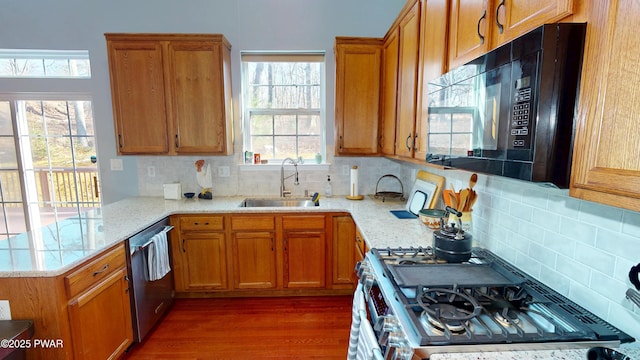 kitchen featuring stainless steel appliances, a peninsula, a sink, and brown cabinetry