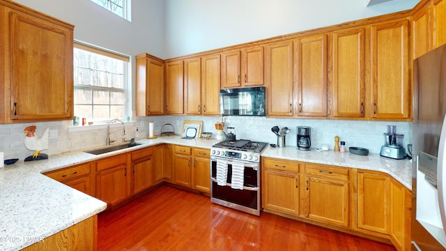 kitchen featuring light stone counters, tasteful backsplash, wood finished floors, a sink, and stainless steel appliances
