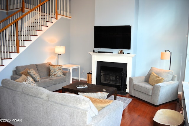 living room with a fireplace with flush hearth, baseboards, wood finished floors, and stairway