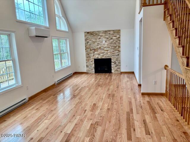 9 Wallenpaupack Dr, Lake Ariel, PA 18436 - unfurnished living room with a baseboard heating unit, a wall unit AC, high vaulted ceiling, light wood-type flooring, and a stone fireplace